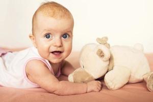 retrato de un pequeño linda bebé acostado en cama con su suave juguete y sonriente. corteza en el del bebe cabeza foto