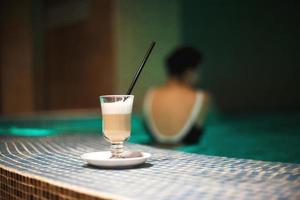 a cup of coffee in the pool and a girl in the background photo