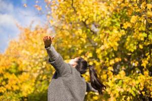 niña en el parque lanza otoño hojas
