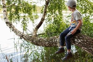 the boy sits on a tree by the lake photo