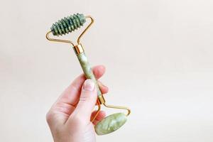 woman holding in hand massage quartz roller for the face of natural nephritis on beige background. photo