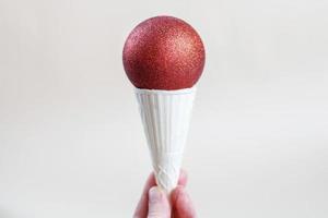 woman holding in hand ice cream cone with red shiny Christmas ball. photo