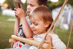 children sitting on a swing with phone photo