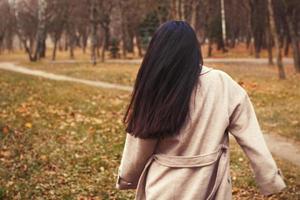 portrait of brunette hair woman in beige coat walking at the city park . photo