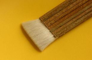 Diagonal cropped view of wooden or bamboo textured handle white brush for cleaning or writing with unusual shape. Object photo isolated on yellow background.