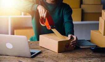 Startup SME small business entrepreneur of freelance Asian woman wearing apron using laptop and box to receive and review orders online to prepare to pack sell to customers, online sme business ideas. photo