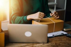 Startup SME small business entrepreneur of freelance Asian woman wearing apron using laptop and box to receive and review orders online to prepare to pack sell to customers, online sme business ideas. photo