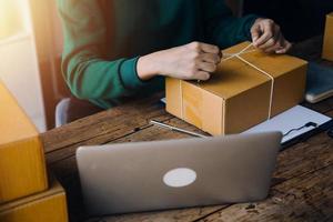 Startup SME small business entrepreneur of freelance Asian woman wearing apron using laptop and box to receive and review orders online to prepare to pack sell to customers, online sme business ideas. photo
