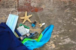 Beach bag, women's accessories, pills and protective medical mask on old wooden background. Top view. photo