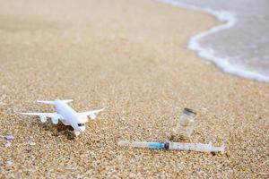 Vaccine against Covid-19, syringe, plane on beach. photo