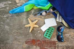 Summer women's beach accessories for your sea holiday and pill on old wooden background. Concept of medication required in journey. Top view. photo