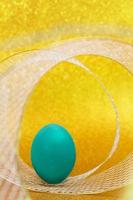 Blue egg stands on swirl mesh ribbon behind yellow shiny background. Vertical. Easter. Copy space photo