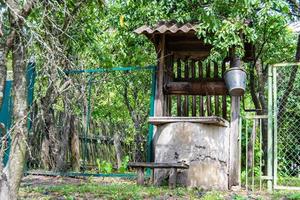 Old well with iron bucket on long forged chain for clean drinking water photo