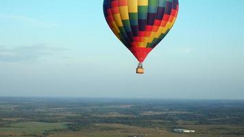 un globo de aire colorido vuela en vuelo libre sobre el campo. vista panorámica. globo multicolor en el cielo azul video