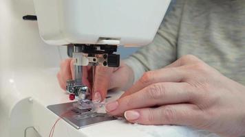 el manos de un de edad mediana mujer coser tela en un moderno de coser máquina. costurera a trabajo video
