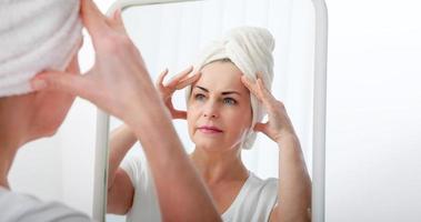 Forty years old woman looking at wrinkles in mirror. Plastic surgery and collagen injections. Selective focus on the face. photo