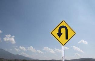 Traffic sign, left U turn sign on cement pole beside the rural road with white cloudy bluesky background, copy space. photo