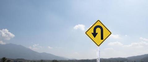 Traffic sign, left U turn sign on cement pole beside the rural road with white cloudy bluesky background, copy space. photo