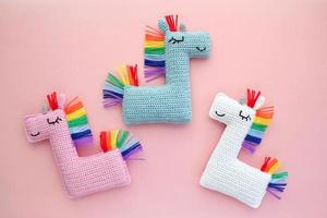 Crochet amigurumi handmade stuffed soft colored unicorn toys with rainbow mane on pink background. Handwork, hobby. Craft diy newborn pregnancy concept. Knitted doll for little baby. Close up flat lay photo