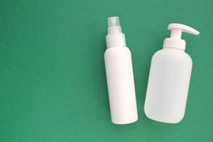 White unbranded plastic dispenser pump and spray bottle on green background with copy space. Cosmetic package mockup, liquid soap flacon, hand sanitizer without label, shampoo organic spa, shower gel photo