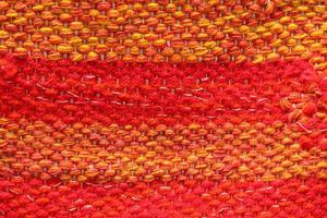Woven red and orange wool fabric texture. Hand knitted textile canvas background. Patchwork carpet backdrop. Factory material threads. Abstract design. Close-up, mockup, top view photo