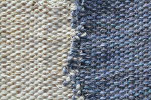 Woven white and blue wool fabric texture. Hand knitted textile canvas background. Patchwork carpet backdrop. Factory material threads. Abstract design. Close-up, mockup, top view photo