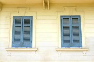 Two blue vintage windows on classic or yellow concrete wall. Exterior design and Wooden object. photo