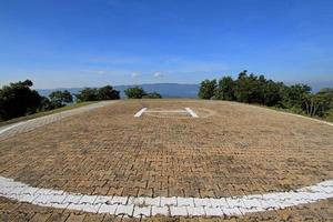 The textured of heliport on the top of high mountain with blue sky and tree background. Transportation and Pattern of tile floor. Place for helicopter parked, landing and take off. photo