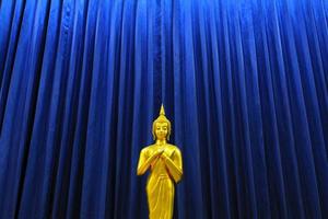 Golden Buddha statue on pattern of blue curtain background. Religion, faith, buddist and Ancient,  Gold object with copy space. photo