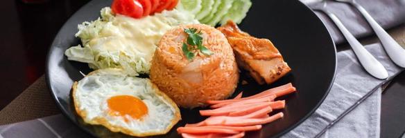 Fried rice, fried egg, cucumber, sliced tomato, green salad and Fried chicken placed on a black plate as a garnish. photo