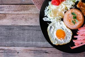 Fried rice, fried egg, cucumber, sliced tomato, green salad and Fried chicken placed on a black plate as a garnish. photo