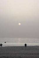 playa solitaria con gente paseando por la arena al borde de las olas del mar foto