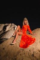 mujer en naranja vestir con Delgado desnudo piernas posando cerca el arena colina foto