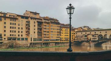 Detail of old town medieval bridge over gloomy waters and yellow buildings with light post in center photo