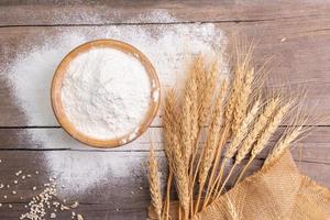 wheat flour in a wooden bowl There are ears of wheat on the table. Old wooden background - top view photo