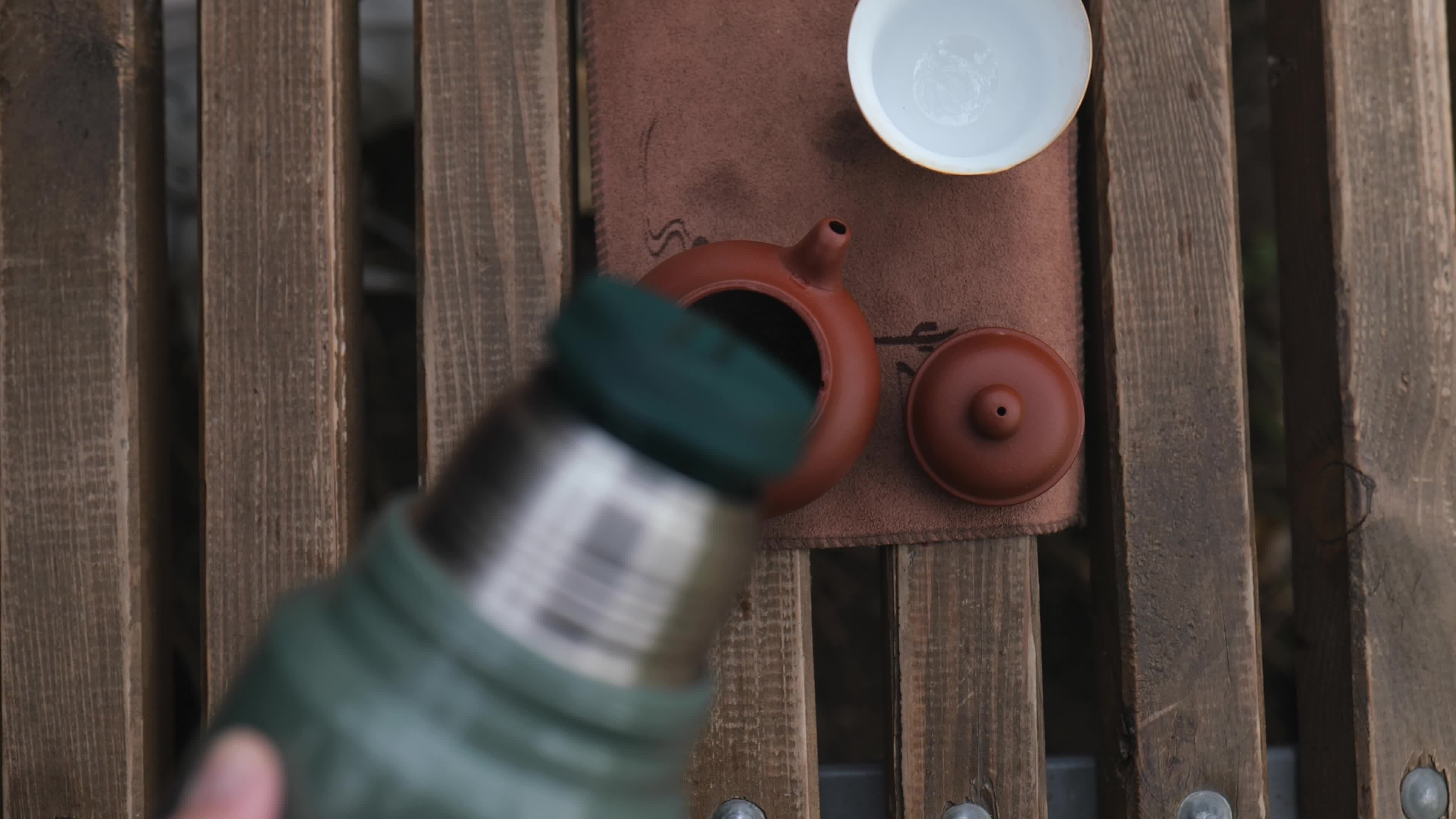 pouring boiling water from a thermos into a clay teapot with tea