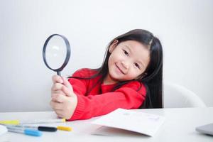 linda asiático niña participación un aumentador vaso en el estudiar escritorio. concepto de educativo desarrollo. foto