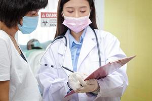 An Asian female doctor explains to his wife the treatment information of an African-American male patient. Concept of medical service in hospital During COVID-19 photo