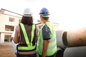 ingenieros y arquitectos, hombres y mujer, Mira a el edificio Plano a cheque el exactitud de el construcción. foto