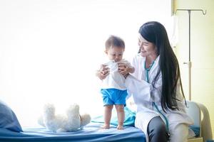 Female doctor examines the Asian little boy patient in bed in a clinic. Health care concept photo