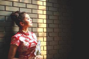 Asian woman wearing a Chinese dress, standing, holding a fan, a backdrop of a black brick wall. Have space to write messages photo