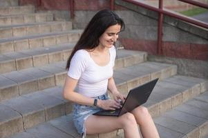 the girl is sitting on the stairs, laptop on her lap, looking into the distance photo