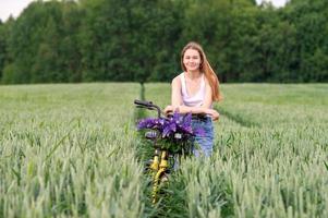 A pretty girl stands with a bouquet of lupines in a field next to a bicycle photo