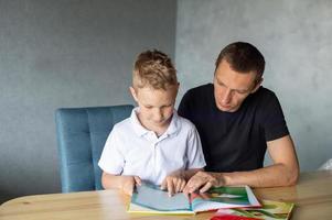 un linda chico es sentado a el mesa con su papá y acecho un libro acerca de serpientes foto