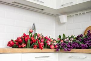 un grande número de tulipanes de diferente colores mentiras en el mesa en el cocina. flores en el lavabo foto