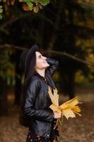 A girl in a black hat holds yellow autumn leaves in her hands photo