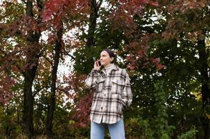 A girl in warm clothes is talking on the phone against the background of the forest and laughing photo