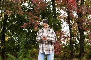 un linda niña soportes en el otoño bosque con un teléfono y escribe un mensaje foto