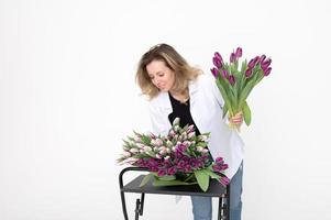 un dulce niña recogido un ramo de flores de diferente variedades de tulipanes soportes en un blanco antecedentes foto