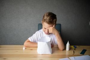 The boy cuts out details from paper. Glue the parts together with glue photo